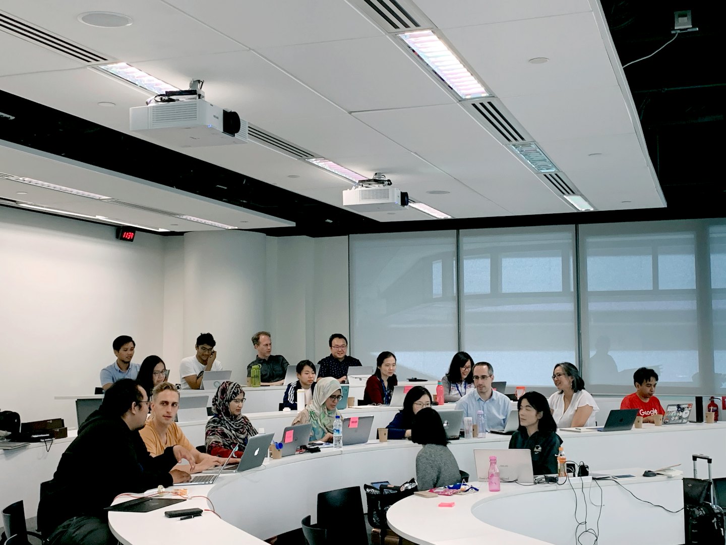 Des adultes diversifiés collaborent et apprennent sur des ordinateurs portables dans une salle de classe moderne.
